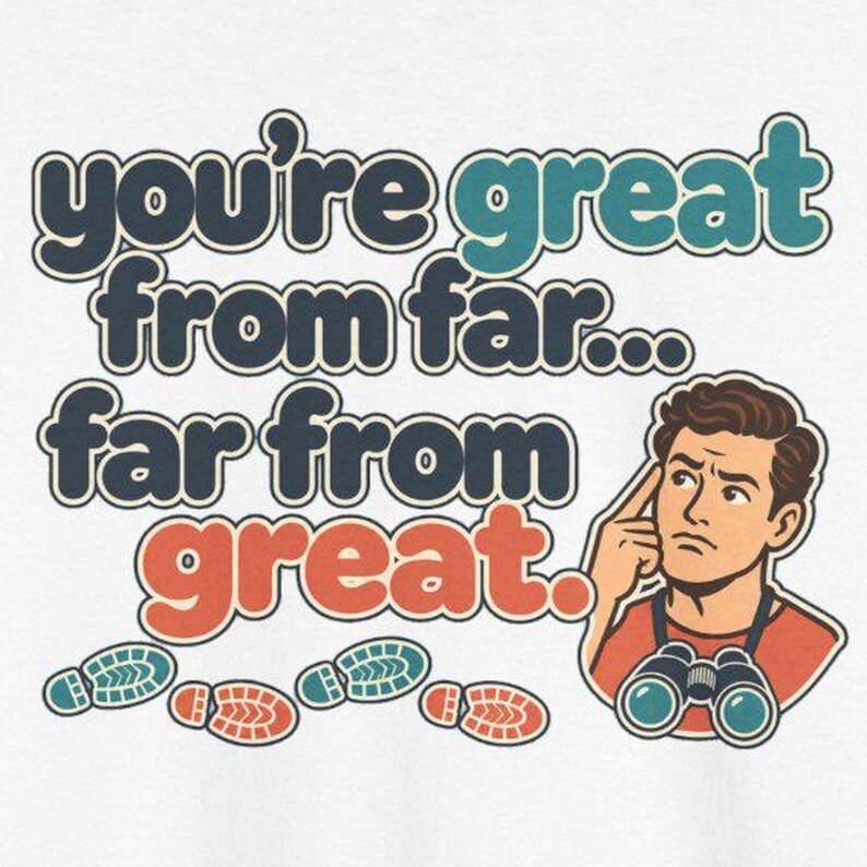 May include: A white t-shirt graphic featuring the text "you're great from far... far from great." in dark blue, teal, and orange. An illustration of a person with brown hair wearing binoculars and pointing to their head is included.