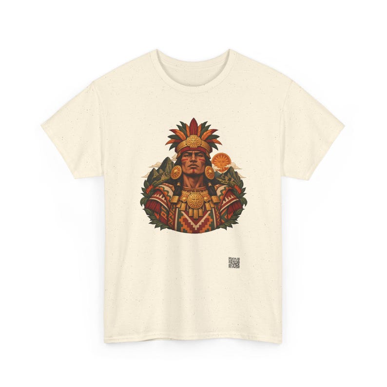 May include: A cream-colored t-shirt featuring a central graphic of a person wearing an elaborate feathered headdress and gold jewelry. The design includes geometric patterns, mountain silhouettes, and a sun, with a small QR code below the image.