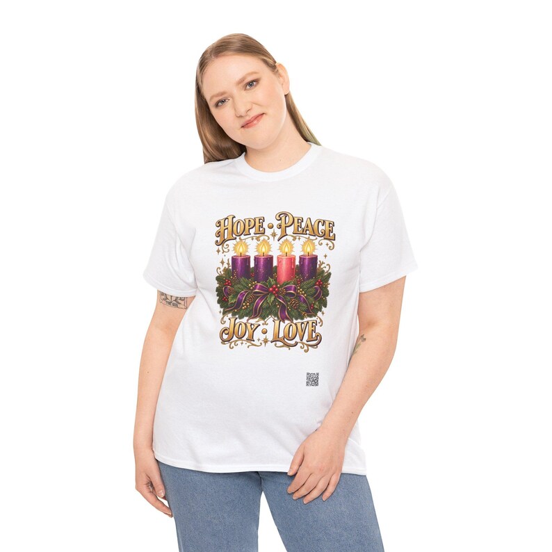 May include: A white t-shirt featuring a graphic of an Advent wreath with four lit candles, three purple and one pink, surrounded by greenery and ribbons. The text reads HOPE, PEACE, JOY, and LOVE in a decorative gold font above and below.