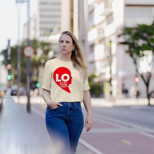 Puede incluir: Una camiseta de manga corta color crema con un gr&aacute;fico rojo en forma de coraz&oacute;n en el pecho. El gr&aacute;fico contiene el texto blanco LO y R U MY OTHER HALF? dentro de la forma del coraz&oacute;n, que est&aacute; dividida para formar la silueta de una cara.