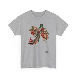 May include: A heather gray t-shirt featuring a central graphic of a quetzal bird perched on a branch with cocoa pods and white flowers. The bird has long, flowing green and red tail feathers with geometric patterns in red, green, and cream.