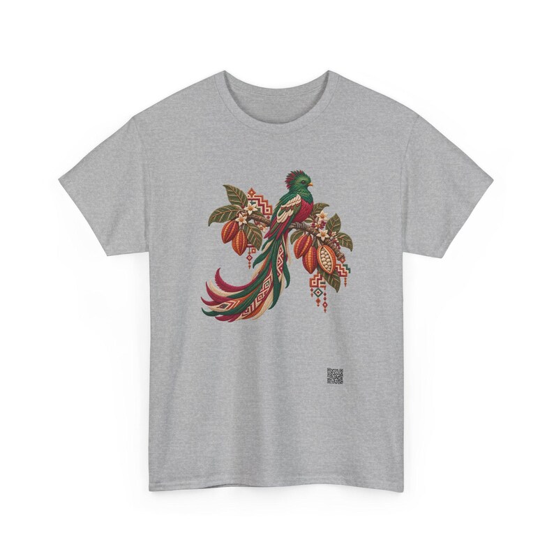 May include: A heather gray t-shirt featuring a central graphic of a quetzal bird perched on a branch with cocoa pods and white flowers. The bird has long, flowing green and red tail feathers with geometric patterns in red, green, and cream.