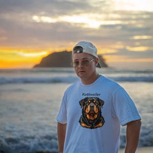 May include: A white short-sleeved t-shirt featuring a graphic illustration of a Rottweiler dog head centered on the chest, with the text "Rottweiler" printed in black lettering directly above the dog's head.