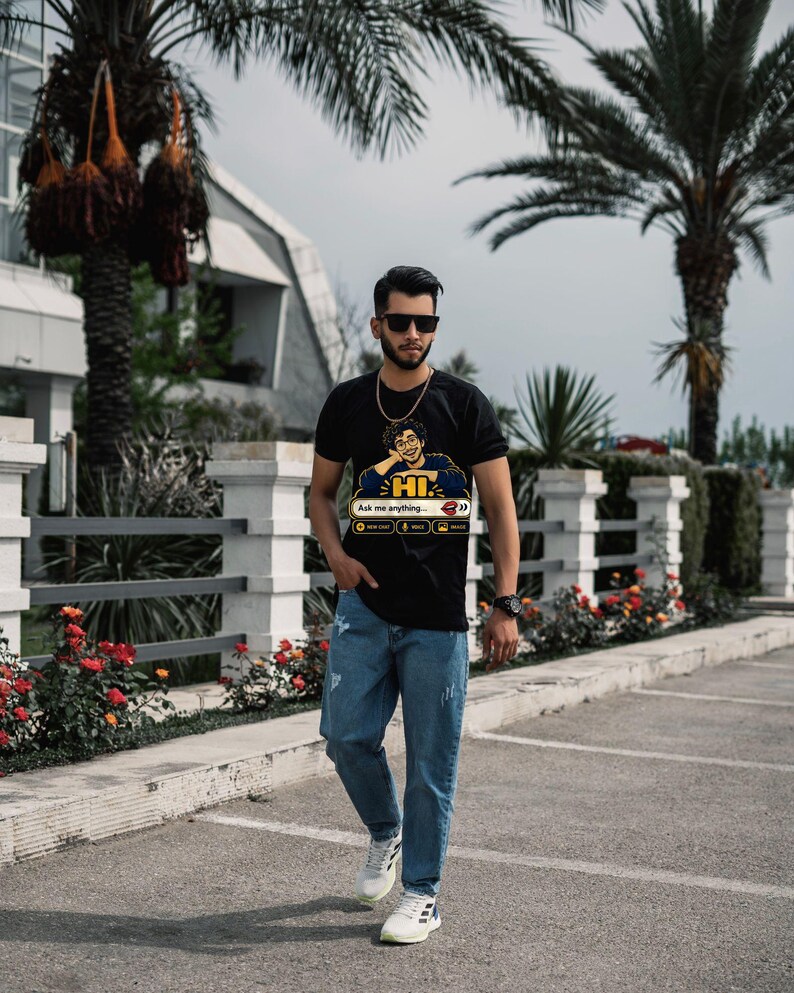 May include: A black short-sleeve t-shirt featuring a graphic of a person resting their chin on their hands with the text "HI" and "Ask me anything" above icons for voice and image, paired with blue denim jeans and white sneakers.