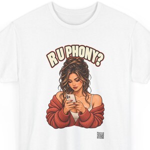 May include: A white t-shirt featuring a graphic illustration of a person with long brown hair in an updo, wearing a white tank top and a chunky red cardigan, looking at a smartphone. The text RU PHONY? is printed in a curved font above the figure.