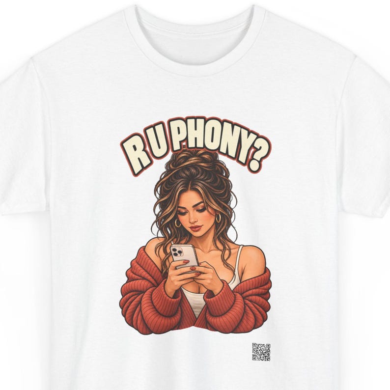 May include: A white t-shirt featuring a graphic illustration of a person with long brown hair in an updo, wearing a white tank top and a chunky red cardigan, looking at a smartphone. The text RU PHONY? is printed in a curved font above the figure.
