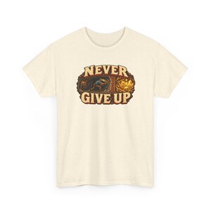 Puede incluir: Una camiseta de manga corta color crema con textura moteada. El gr&aacute;fico central muestra a un minero trabajando en un t&uacute;nel con cristales de oro, rodeado por el texto NEVER GIVE UP en letras marrones en negrita.