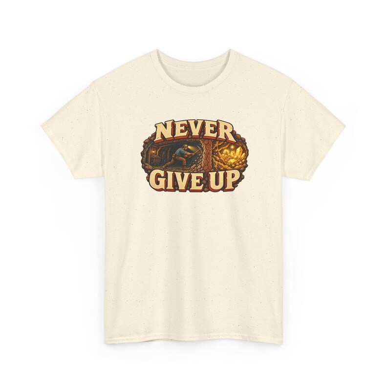Puede incluir: Una camiseta de manga corta color crema con textura moteada. El gr&aacute;fico central muestra a un minero trabajando en un t&uacute;nel con cristales de oro, rodeado por el texto NEVER GIVE UP en letras marrones en negrita.