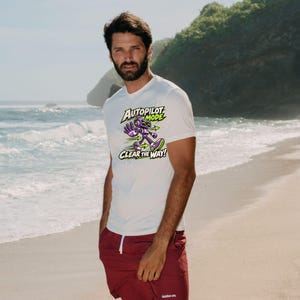 May include: A white short-sleeved t-shirt featuring a graphic of a purple robot with green accents and the text "AUTOPILOT MODE CLEAR THE WAY!" paired with solid maroon shorts that have a white drawstring and a small white logo on the leg.