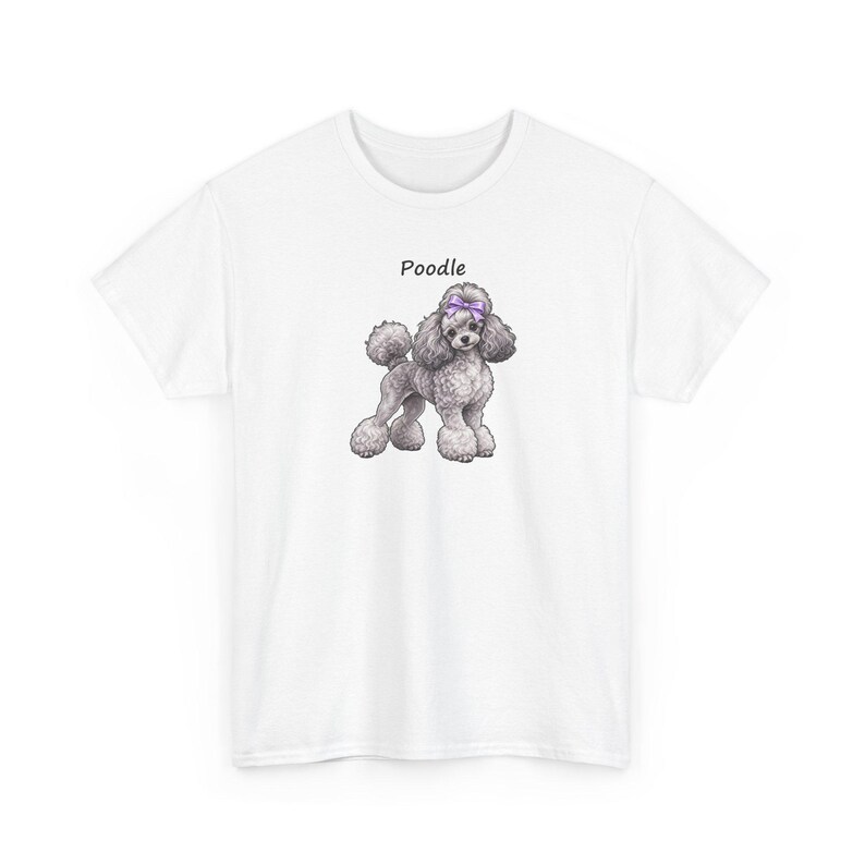 May include: A white short-sleeved t-shirt featuring a centered graphic of a grey poodle dog with a purple bow on its head. The word Poodle is printed in black text above the illustration of the dog, which has curly fur and a pom-pom tail.