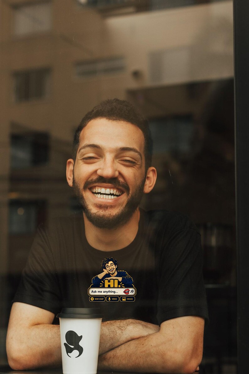 May include: A black short-sleeved t-shirt featuring a graphic of a person with glasses resting their chin on their hand above the text HI and Ask me anything, with icons for new chat, voice, and image, plus a white coffee cup with a black logo.
