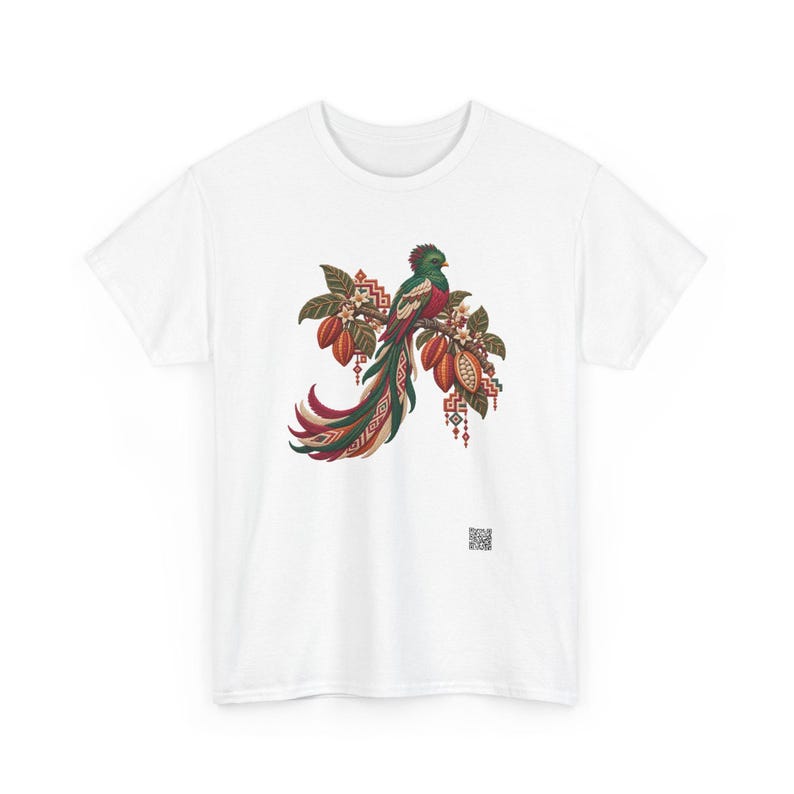 May include: A white short-sleeve t-shirt featuring a central graphic of a quetzal bird perched on a branch with cacao pods and leaves. The design incorporates geometric patterns in red, green, and brown, with a small QR code near the bottom.
