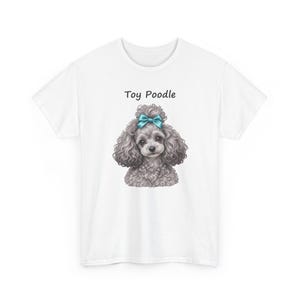 K&ouml;nnte beinhalten: Ein wei&szlig;es T-Shirt mit kurzen &Auml;rmeln und einer Grafik eines grauen, lockigen Toypudels mit einer leuchtend blauen Schleife auf dem Kopf. Der Text Toy Poodle ist in Schwarz &uuml;ber der Hundeillustration auf der Brust des Shirts aufgedruckt.