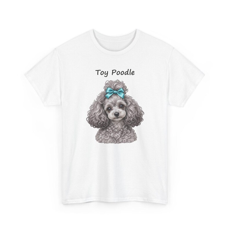 K&ouml;nnte beinhalten: Ein wei&szlig;es T-Shirt mit kurzen &Auml;rmeln und einer Grafik eines grauen, lockigen Toypudels mit einer leuchtend blauen Schleife auf dem Kopf. Der Text Toy Poodle ist in Schwarz &uuml;ber der Hundeillustration auf der Brust des Shirts aufgedruckt.
