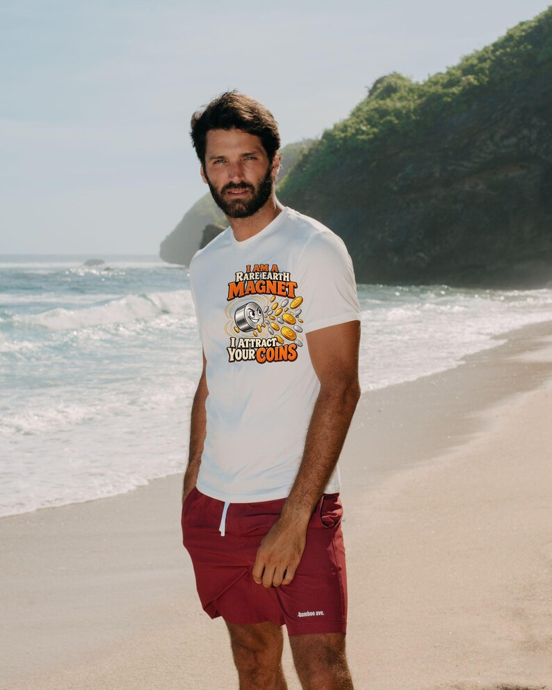 May include: A white short-sleeved t-shirt featuring a graphic of a magnet attracting gold and silver coins with the text I AM A RARE EARTH MAGNET I ATTRACT YOUR COINS, paired with solid maroon shorts featuring a white drawstring.