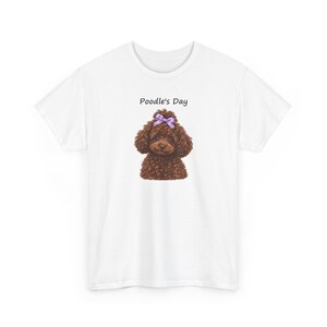May include: A white short-sleeved t-shirt featuring a graphic of a brown curly-haired poodle with a light purple bow on its head. Above the dog illustration, the text Poodle's Day is printed in a simple black sans-serif font.