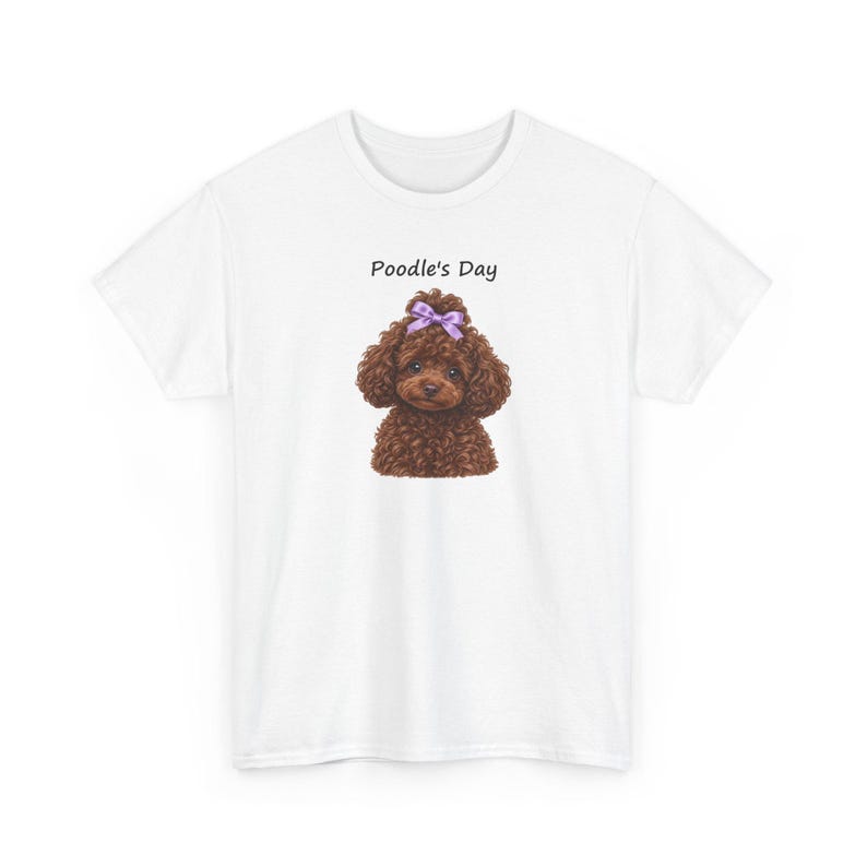 May include: A white short-sleeved t-shirt featuring a graphic of a brown curly-haired poodle with a light purple bow on its head. Above the dog illustration, the text Poodle's Day is printed in a simple black sans-serif font.