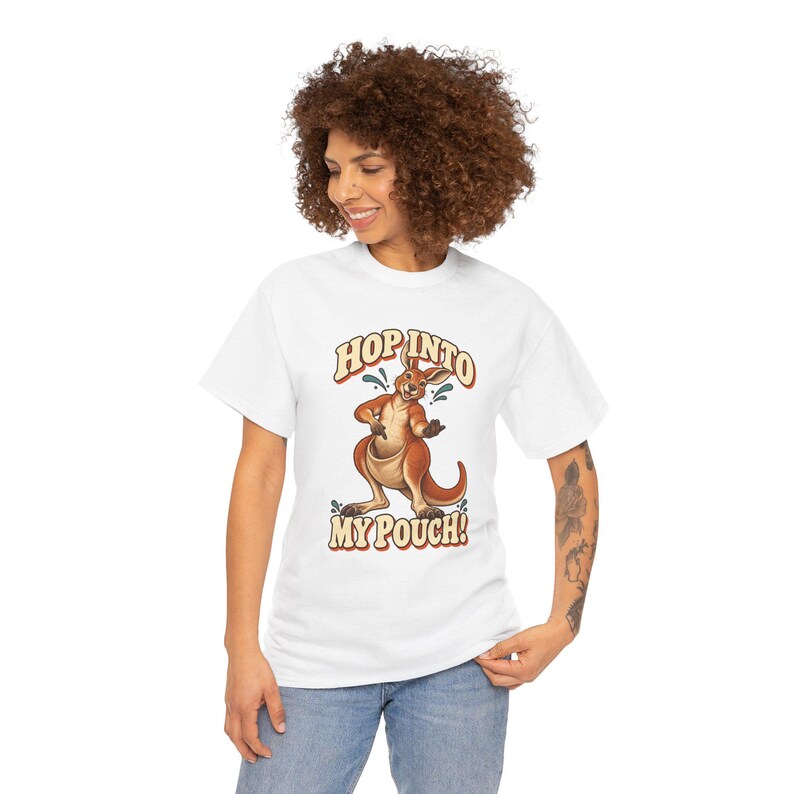 Puede incluir: Una camiseta blanca de manga corta con un gr&aacute;fico de un canguro marr&oacute;n de pie. El texto "HOP INTO MY POUCH!" est&aacute; impreso en una fuente de estilo retro encima y debajo de la ilustraci&oacute;n del canguro, que incluye peque&ntilde;os acentos azules.