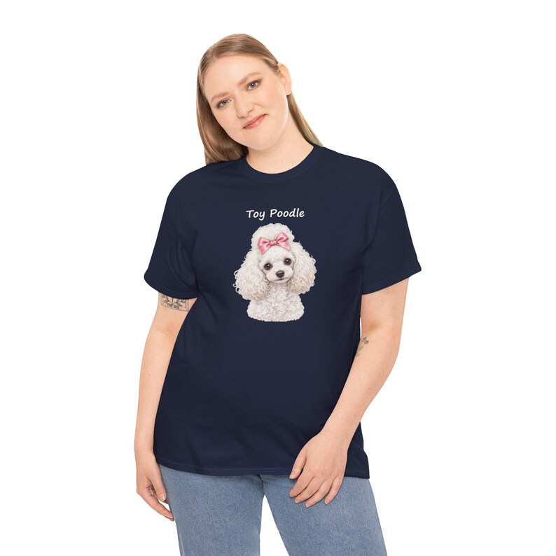 May include: A navy blue short-sleeve t-shirt featuring a graphic of a white toy poodle with a pink bow on its head. The text Toy Poodle is printed in white above the dog illustration. The shirt has a crew neckline and a standard fit.