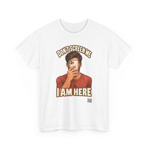 Op de afbeelding: Een wit t-shirt met een afbeelding van een persoon in een roestkleurig shirt die een smartphone voor het gezicht houdt. De tekst erboven luidt DON'T SCREEN ME en de tekst eronder I AM HERE, met een kleine QR-code rechtsonder.