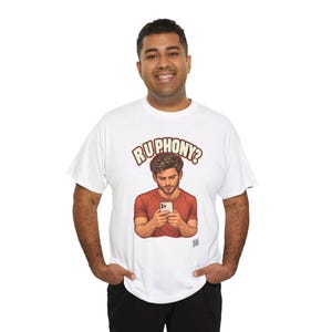 May include: A white short-sleeve t-shirt featuring a graphic illustration of a person in a red shirt looking down at a smartphone. Above the illustration, the text "RU PHONY?" is printed in a bold, cream-colored font with a dark red outline.