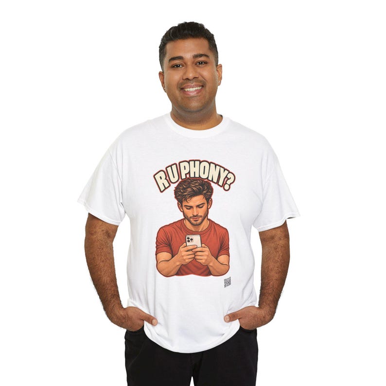 May include: A white short-sleeve t-shirt featuring a graphic illustration of a person in a red shirt looking down at a smartphone. Above the illustration, the text "RU PHONY?" is printed in a bold, cream-colored font with a dark red outline.