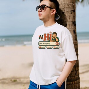 Puede incluir: Una camiseta blanca de manga corta con un estampado gr&aacute;fico de una interfaz de chat con el texto "AI HI" y "Ask me anything..." junto a iconos de chat, voz e imagen, combinada con pantalones cortos azules con cord&oacute;n.
