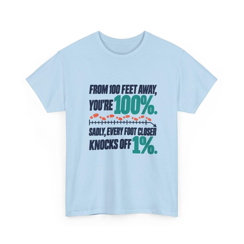 May include: A light blue t-shirt featuring dark navy and teal text that reads: FROM 100 FEET AWAY, YOU'RE 100%. SADLY, EVERY FOOT CLOSER KNOCKS OFF 1%. The design includes a horizontal line with small orange footprints above it.