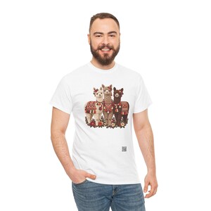 May include: A white short-sleeved t-shirt featuring a graphic print of three llamas standing together. The llamas are adorned with colorful patterned blankets, tassels, and floral headpieces. A small QR code is printed near the bottom right.
