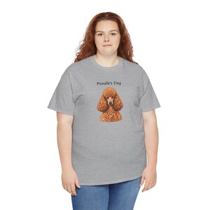 May include: A heather gray short-sleeve t-shirt featuring a graphic of a brown poodle dog centered on the chest. Above the dog illustration, the text Poodle's Day is printed in a simple black sans-serif font. The shirt has a crew neckline.