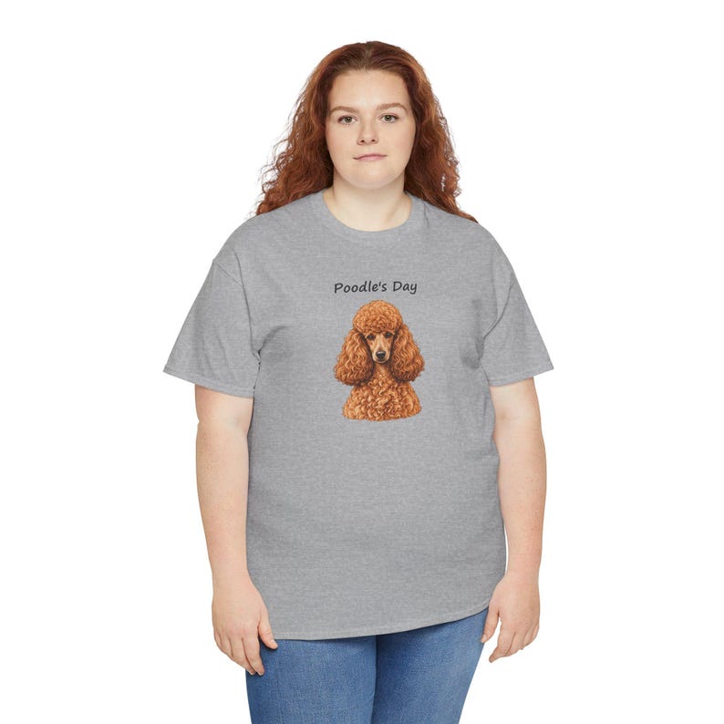 May include: A heather gray short-sleeve t-shirt featuring a graphic of a brown poodle dog centered on the chest. Above the dog illustration, the text Poodle's Day is printed in a simple black sans-serif font. The shirt has a crew neckline.