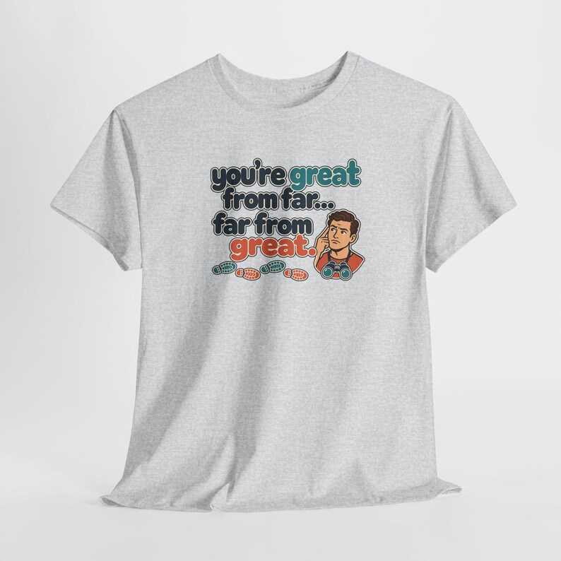 May include: A light gray short-sleeved t-shirt featuring the text "you're great from far... far from great." alongside an illustration of a person looking through binoculars and four small colorful footprints below the text.