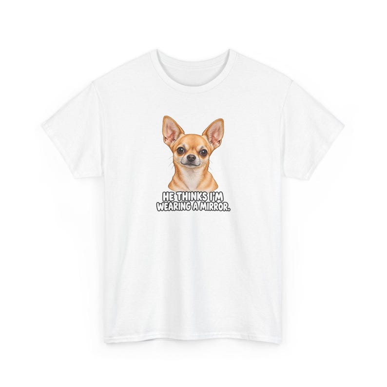 May include: A white short-sleeved t-shirt featuring a graphic of a tan Chihuahua dog centered on the chest. Below the dog, the text reads HE THINKS I'M WEARING A MIRROR in bold, black, uppercase letters with a white outline.