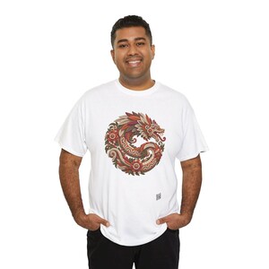 Puede incluir: Una camiseta blanca de manga corta con un gr&aacute;fico circular en el pecho. El dise&ntilde;o muestra un drag&oacute;n estilizado enroscado en un c&iacute;rculo, representado en tonos rojos, naranjas, marrones y crema con intrincados patrones florales.