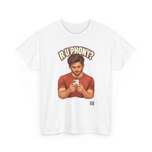 May include: A white short-sleeved t-shirt featuring a graphic of a person with brown hair wearing a red shirt and looking down at a smartphone. Above the figure, the text reads RU PHONY? in bold, arched letters. A small QR code is printed below.