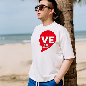 Puede incluir: Una camiseta blanca de manga corta con un gr&aacute;fico rojo en forma de coraz&oacute;n en el pecho. El gr&aacute;fico incluye la silueta de un rostro y el texto blanco VE R WE FULL HEART?. La camiseta se combina con pantalones cortos azules y gafas de sol negras.