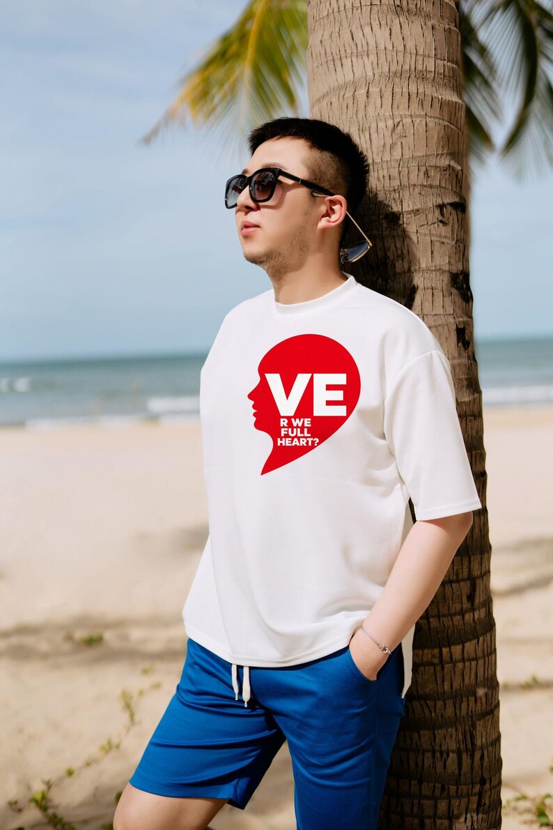 Puede incluir: Una camiseta blanca de manga corta con un gr&aacute;fico rojo en forma de coraz&oacute;n en el pecho. El gr&aacute;fico incluye la silueta de un rostro y el texto blanco VE R WE FULL HEART?. La camiseta se combina con pantalones cortos azules y gafas de sol negras.