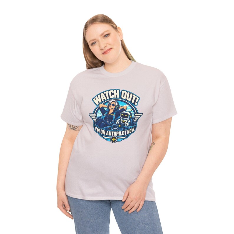 May include: A light gray short-sleeve t-shirt featuring a graphic print of a pilot and a small robot in a cockpit. The text reads WATCH OUT! I'M ON AUTOPILOT NOW. The design is circular with blue and white accents and a small airplane icon.