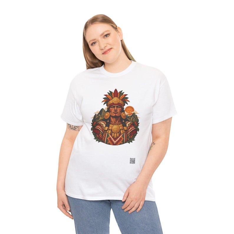 May include: A white short-sleeved t-shirt featuring a central graphic of a person wearing an elaborate feathered headdress and traditional patterned clothing, with a small square QR code printed near the bottom hem of the shirt.