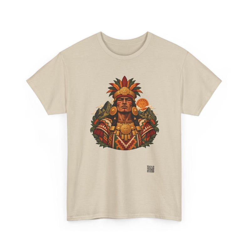 May include: A beige short-sleeved t-shirt featuring a central graphic of a person wearing a feathered headdress and ornate gold jewelry. The design includes mountain silhouettes, a sun, and geometric patterns in red, green, and gold.