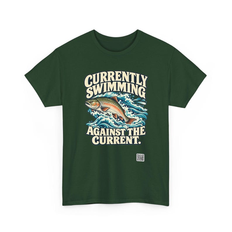 May include: A dark green t-shirt featuring a graphic of a trout jumping through blue waves. The text above the fish reads "CURRENTLY SWIMMING" and the text below reads "AGAINST THE CURRENT." A small square QR code is printed near the bottom.