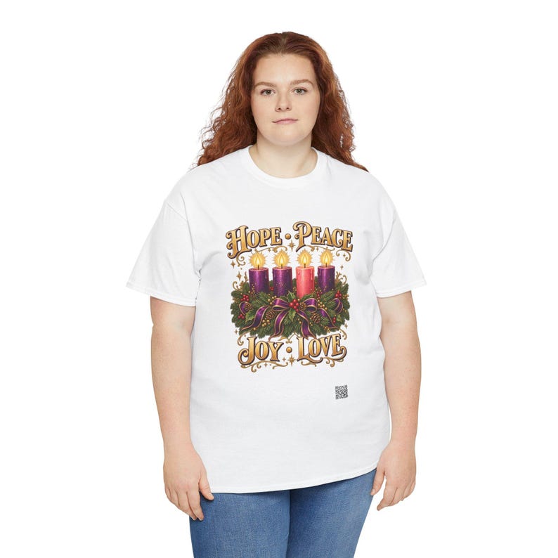 May include: A white t-shirt featuring a graphic of an Advent wreath with four lit candles, three purple and one pink, surrounded by greenery and ribbons. The text "HOPE PEACE" appears above the candles, and "JOY LOVE" appears below in gold.