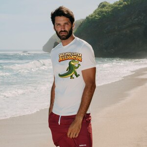 May include: A white short-sleeved t-shirt featuring a graphic of a green alligator waving and the text "SEE YOU LATER ALLIGATOR" in orange and yellow letters, paired with solid maroon shorts with a white drawstring and small white logo.