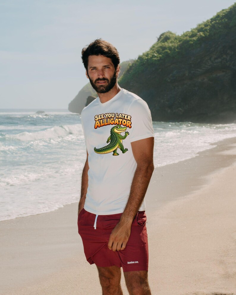 May include: A white short-sleeved t-shirt featuring a graphic of a green alligator waving and the text "SEE YOU LATER ALLIGATOR" in orange and yellow letters, paired with solid maroon shorts with a white drawstring and small white logo.