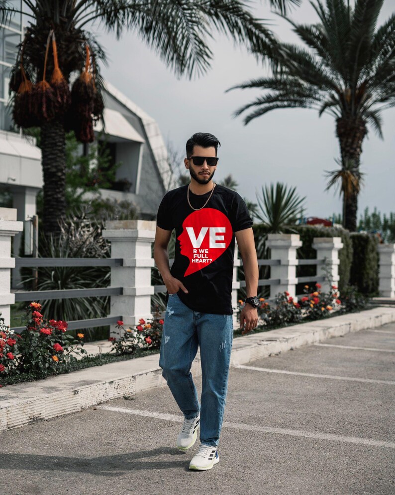 Puede incluir: Una camiseta negra de manga corta con un gr&aacute;fico rojo en forma de coraz&oacute;n en el pecho. El gr&aacute;fico incluye el texto blanco VE, R WE, FULL y HEART? dispuesto verticalmente. La camiseta se combina con vaqueros azul claro y zapatillas blancas.