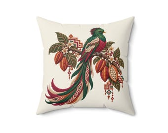 May include: A square throw cushion with an off-white background featuring a detailed illustration of a quetzal bird perched on a branch with cacao pods, green leaves, and white flowers, accented by geometric patterns in red, green, and gold.