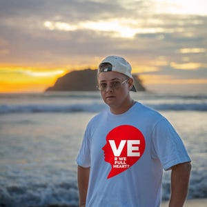 Puede incluir: Una camiseta blanca de manga corta con un gr&aacute;fico rojo de una silueta de cabeza humana integrada en forma de coraz&oacute;n. El gr&aacute;fico incluye el texto blanco VE, R WE FULL HEART? impreso dentro de la forma roja. Tiene cuello redondo.