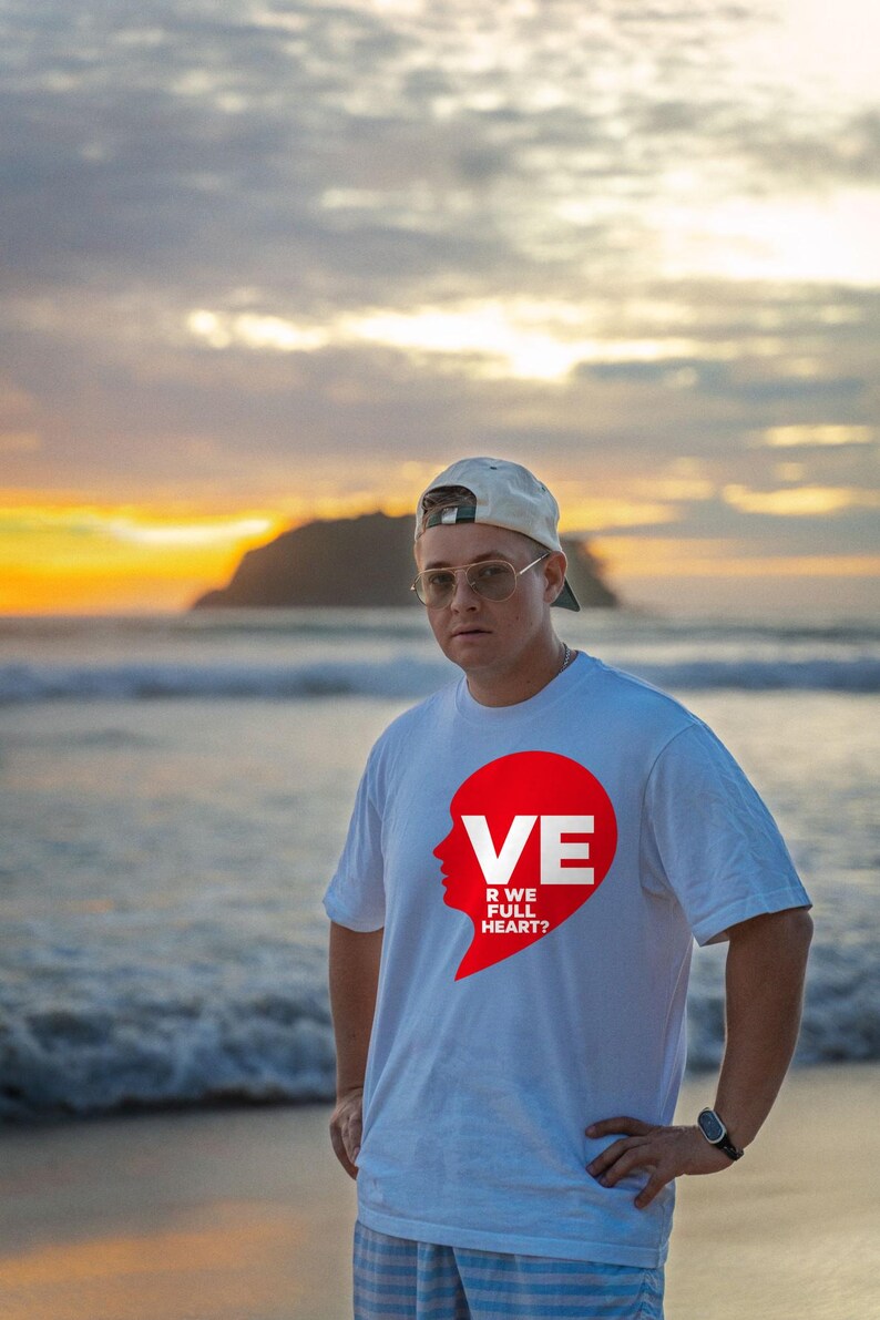 Puede incluir: Una camiseta blanca de manga corta con un gr&aacute;fico rojo de una silueta de cabeza humana integrada en forma de coraz&oacute;n. El gr&aacute;fico incluye el texto blanco VE, R WE FULL HEART? impreso dentro de la forma roja. Tiene cuello redondo.