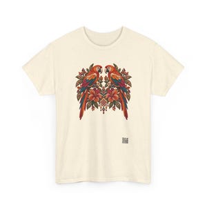 May include: A cream-colored short-sleeve t-shirt featuring a central graphic of two symmetrical parrots perched on branches surrounded by hibiscus flowers and foliage. A small square QR code is printed near the bottom right hem.