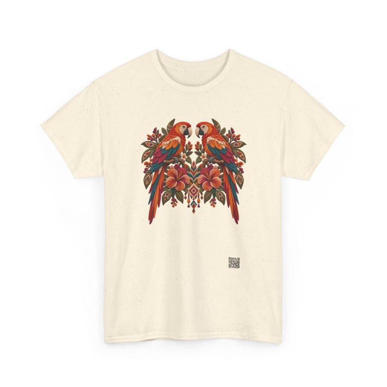 May include: A cream-colored short-sleeve t-shirt featuring a central graphic of two symmetrical parrots perched on branches surrounded by hibiscus flowers and foliage. A small square QR code is printed near the bottom right hem.
